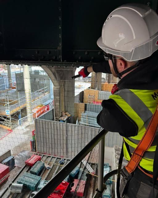 A JR Bird Management technician in a hard hat and harness fitting netting at height
